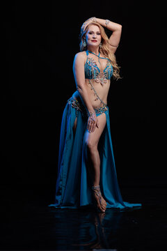 Young woman belly dancer in a blue oriental costume on a black background