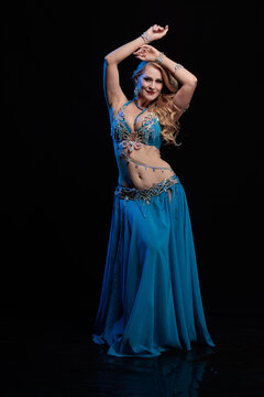 Young woman belly dancer in a blue oriental costume on a black background