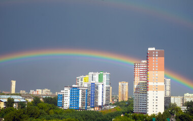 Rainbow in the sky after a thunderstorm in the city. High-rise buildings, lots of greenery