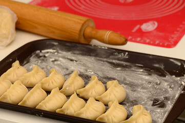 Homemade dumplings arranged neatly on a baking tray with a rolling pin in a cozy kitchen setting