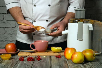Making sweet apple juice by hand chef. Adding sugar with wooden spoon to mug with juice. Juice from apples in the kitchen with juicer