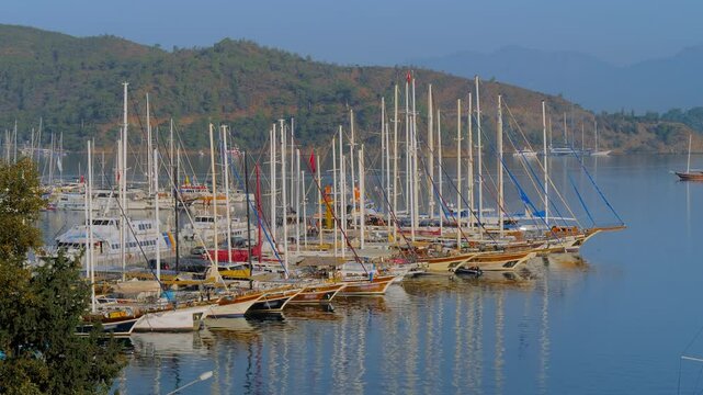 Time lapse: moored gulets and yachts in calm harbor with a scenic hillside backdrop in Fethiye, Turkey. Fast ripples on the sea water surface. Peaceful maritime travel, leisure and timelapse concept