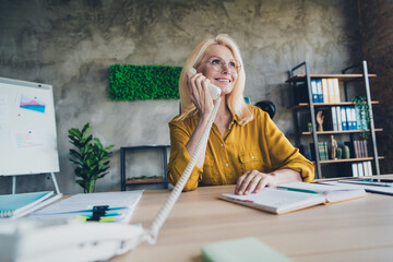 Photo of adorable positive lady broker wear shirt talking land line phone indoors workplace workshop