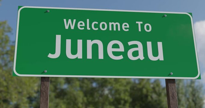 Driving By A Welcome To Juneau, Alaska Green Road Sign Against a Blue Sky and Clouds - United States Capital Series.