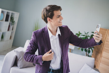 Young man wearing a stylish purple blazer takes a cheerful selfie while relaxing at home in a...