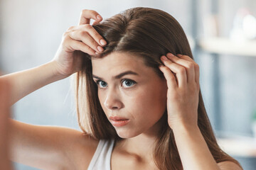 Fototapeta premium Millennial girl with hair loss problem looking in mirror at home