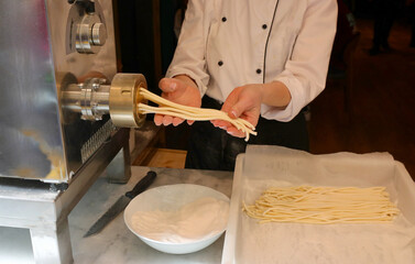pasta maker during the process of extruding fresh egg pasta and the machine that produces thick...
