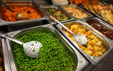 steel trays with peas, baked potatoes, mixed vegetables and other dishes in the cafeteria