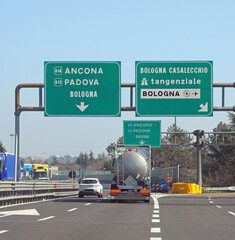 highway signs on the Italian road with the junction to go to Ancona, Padua, Bologna or the ring road and airport and cars and a tanker