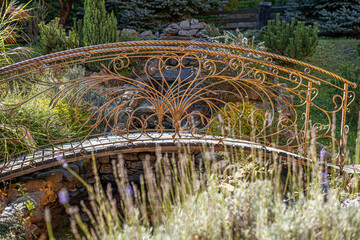 A beautifully crafted wrought iron bridge with intricate golden detailing spans a small garden...