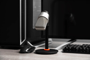 A professional condenser microphone on a desktop stand is set up in a modern gaming and recording...