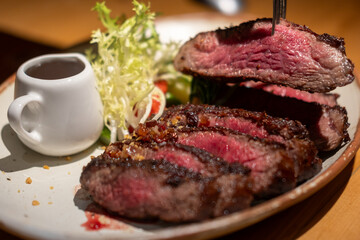 A fork on medium rare wagyu meat served on plate with sauce and vegetable