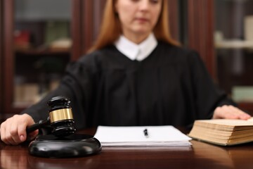 Judge with document striking gavel at wooden table in office, selective focus