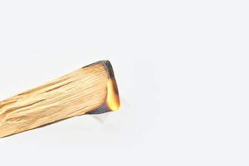 Ignited palo santo stick with small flame against white background.