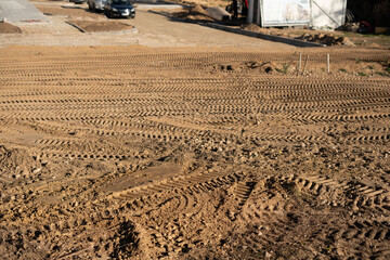 photo Freshly leveled construction site ground displaying intricate tire tracks from heavy...