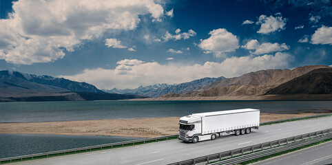 A large white semi truck is driving down a road near a lake