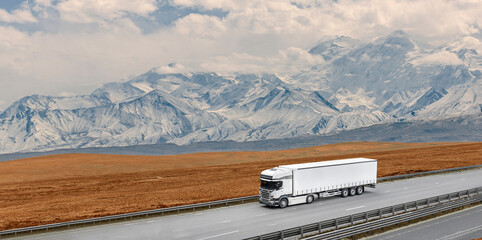 A large white semi truck is driving down a road in front of a mountain range