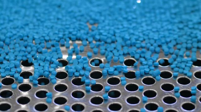 Plastic recycling machine: blue propylene or polyethylene pellets, recycled plastic granules on vibrating shale shaker, conveyor belt: close up. Separation, sustainable and waste reduction concept