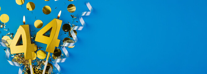 Celebrating 44 years. Golden burning candle in form of number forty four on celebration festive blue background lying in sparkles. Holiday banner