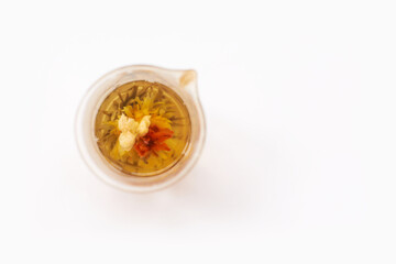 Top view of blooming flower tea in glass teapot with herbal infusion on white background.