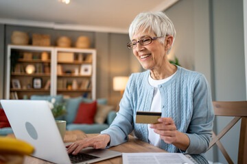 Happy senior woman using laptop and credit card for online shopping at home