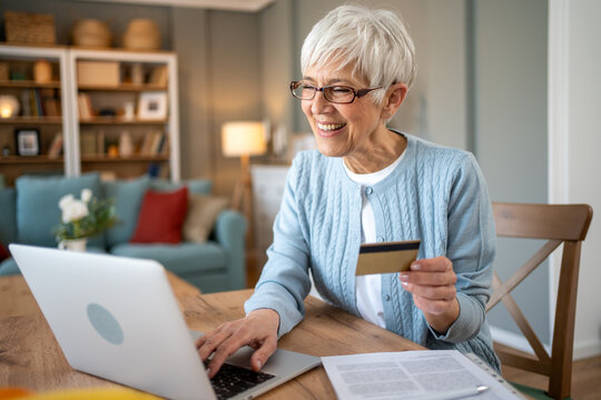 Happy senior woman using laptop and credit card for online shopping at home