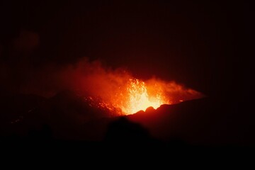 A volcano erupts at night with glowing lava and smoke creating a dramatic fiery landscape