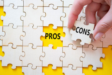 Fototapeta premium Pros vs Cons symbol. Concept word Pros vs Cons on wooden puzzle. Businessman hand. Beautiful yellow background. Business and Pros vs Cons concept. Copy space