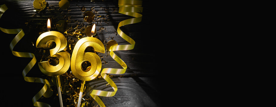 Golden candle shaped as number 36 burns on dark table, surrounded by shimmering confetti and curling ribbons, creating festive atmosphere. Concept of celebrating milestone birthday