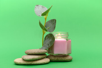 Aromatic candle, stones, green eucalyptus branch. On a green background.