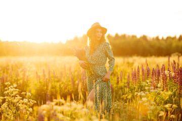 Smiling woman having fun at sunset in purple flowers field. Beautiful woman with wildflower bouquet enjoying nature. Relaxation, posing concept.
