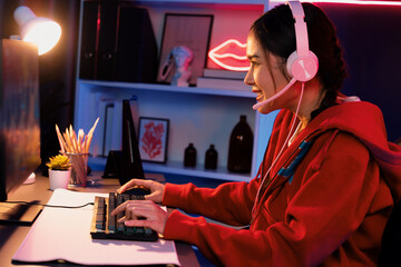 Host channel of smiling beautiful Asian girl streamer playing online game wearing headphone talking with viewers media online recording phone. Esport skilled team players in neon blue room. Stratagem.