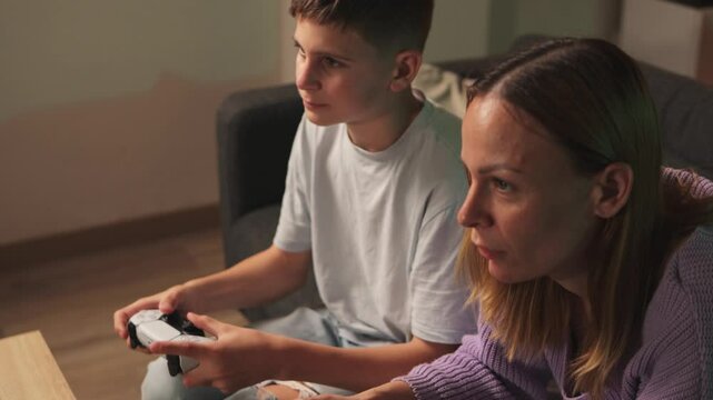 Mother and son closely bonding, playing video game together on living room couch, sharing joyful entertainment moment.People playing console controller, games challenge and entertainment