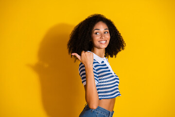 Young cheerful woman with curly hair in stylish striped top smiling against vibrant yellow...