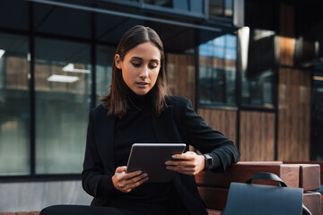 Beautiful brunette businesswoman holding a digital tablet. Young female reading from digital tablet outside.