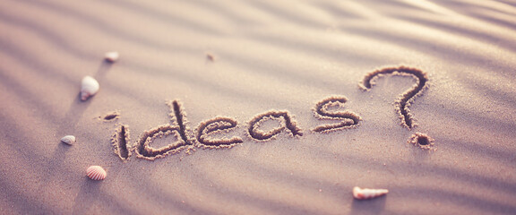 Sand texture with "ideas?" written on beach, surrounded by seashells, evokes contemplation, creativity, and brainstorming concepts, perfect for inspirational content