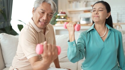 Obraz premium Happy elderly couple exercising together with dumbbells at home, focusing on muscle strength, joint health, and physical wellness for improved mobility and healthy aging. Retirement concept. Myrmidon.