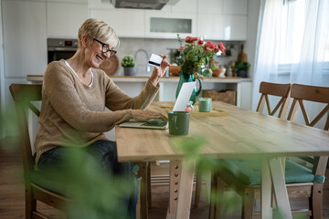 Senior woman using laptop and credit card for online shopping at home