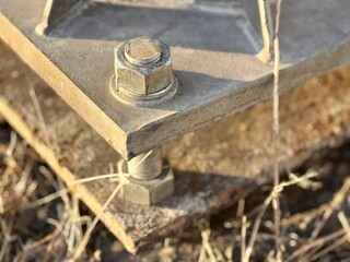 A metal pole attached to the foundation with anchor bolts and nuts. The metal surface of the post and the fastenings are in place. The support of an iron pole for lighting on the street in the park