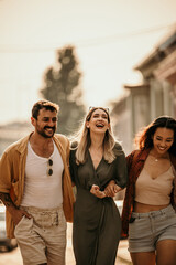 Diverse group of stylish friends laughing and strolling down a sunlit city street