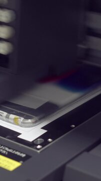 Modern, automated printer creating designs on a phone case, highlighting advanced technology in business production. Printing device concept. Vertical video.