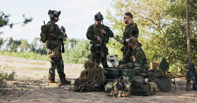 A military unit finalizes mission details, preparing for a forest expedition by analyzing maps, entering data on the computer, sending updates to base, and securing gear.