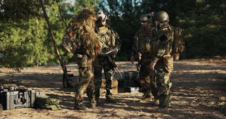 Military troops in camouflage uniforms and helmets secure the base area, carrying long rifles and...