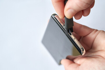 Person cleaning smartphone charging port with brush for maintenance and better functionality.