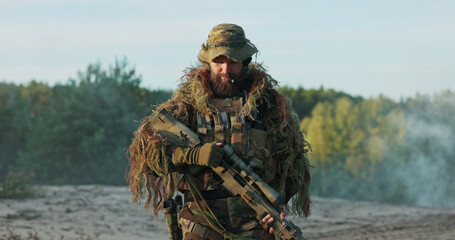 A determined soldier in camouflage uniform and helmet unholsters his rifle, standing tall at...