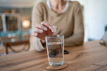 Senior woman taking effervescent pill with glass of water at home