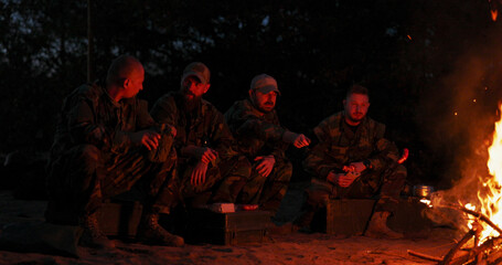 Soldiers establish a nighttime camp in the training area, standing around a fire for warmth,...