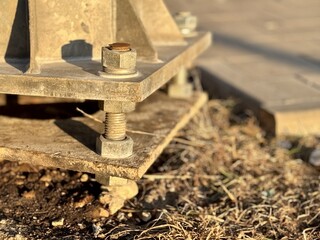 A metal pole attached to the foundation with anchor bolts and nuts. The metal surface of the post and the fastenings are in place. The support of an iron pole for lighting on the street in the park