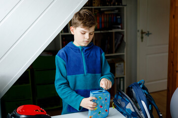 School kid boy getting ready in the morning for school. Healthy child filling satchel with books,...