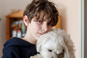Happy teenager boy and cute maltese puppy together. Handsome child holding his dog at home,...